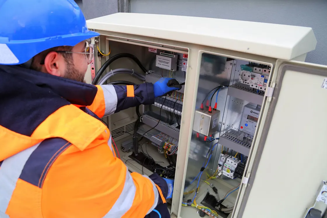 An electrical worker in protective equipment beside an outdoor control panel
