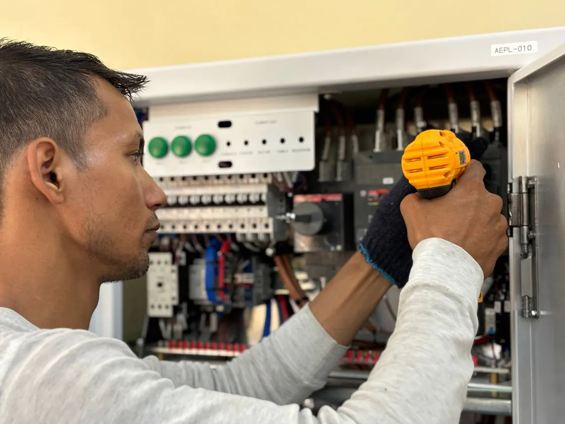 A worker using a drill beside an electrical panel