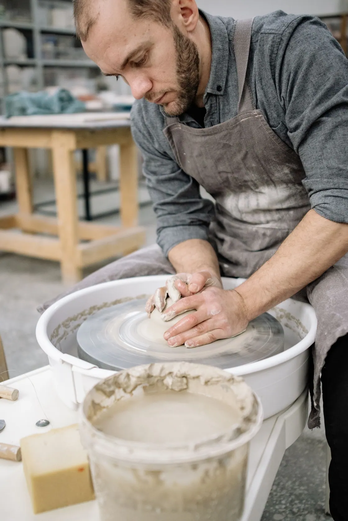 A potter shaping a clay vessel at a workshop table