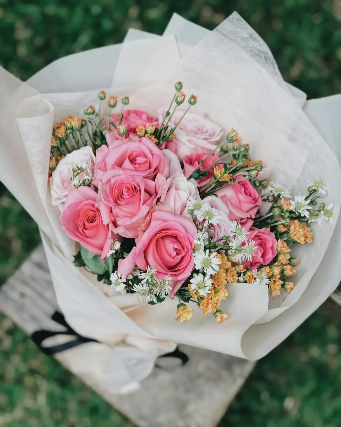 Pink roses and smaller flowers gathered in a wrapped bouquet