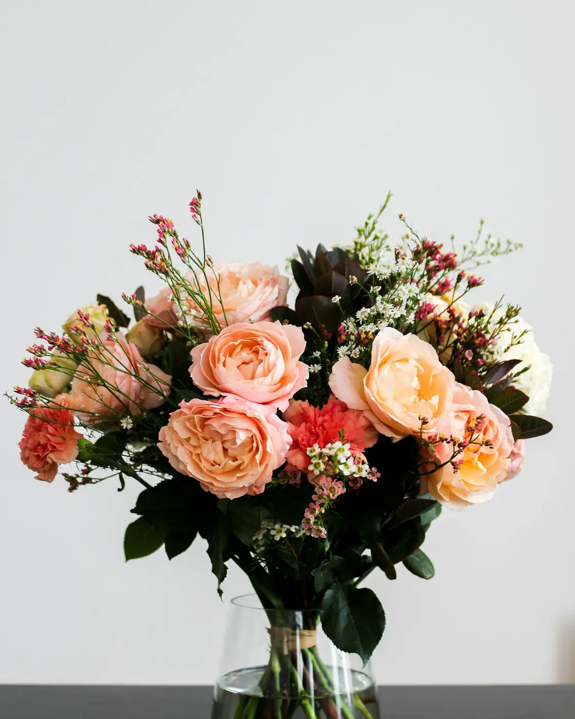 Peach roses and mixed flowers arranged in a glass vase