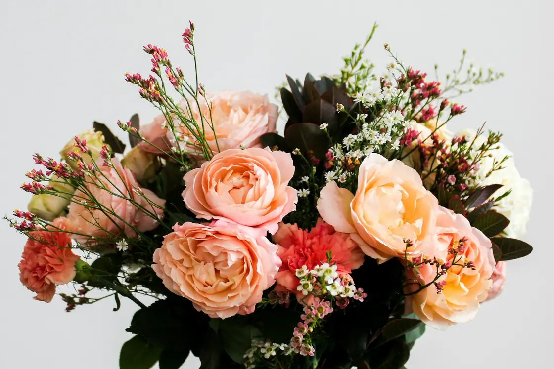 Peach roses and mixed flowers arranged in a glass vase