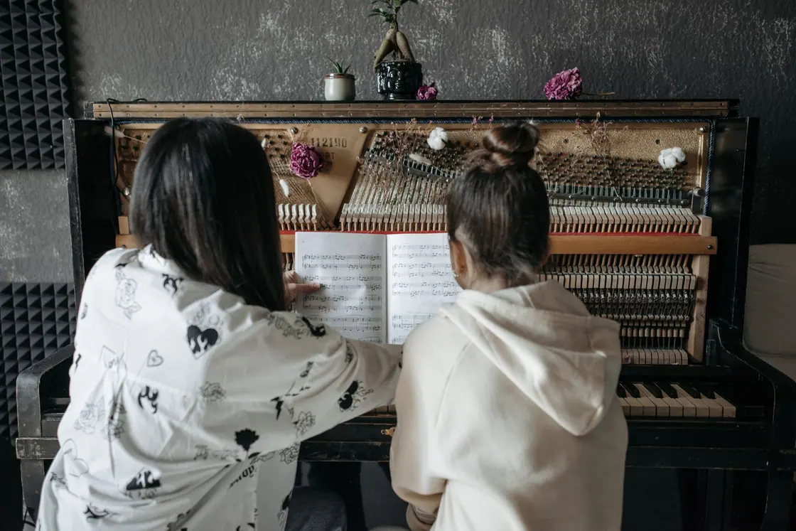A teacher guiding a student at a piano, seen from behind