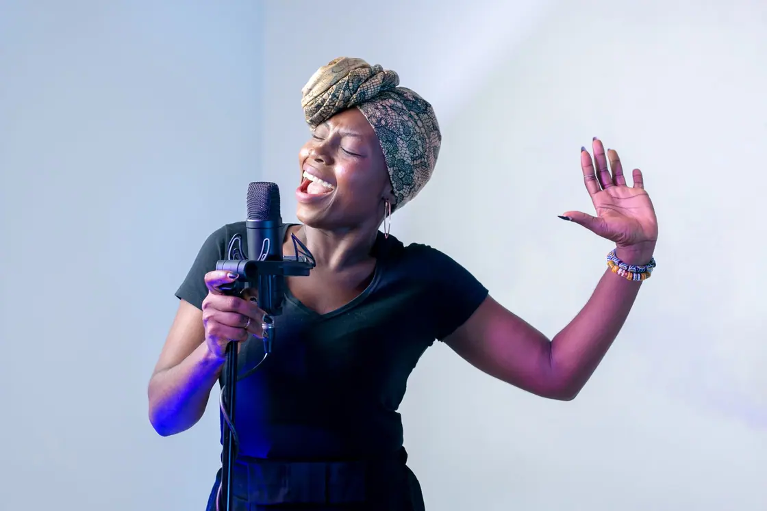 An adult singing into a microphone in a recording studio