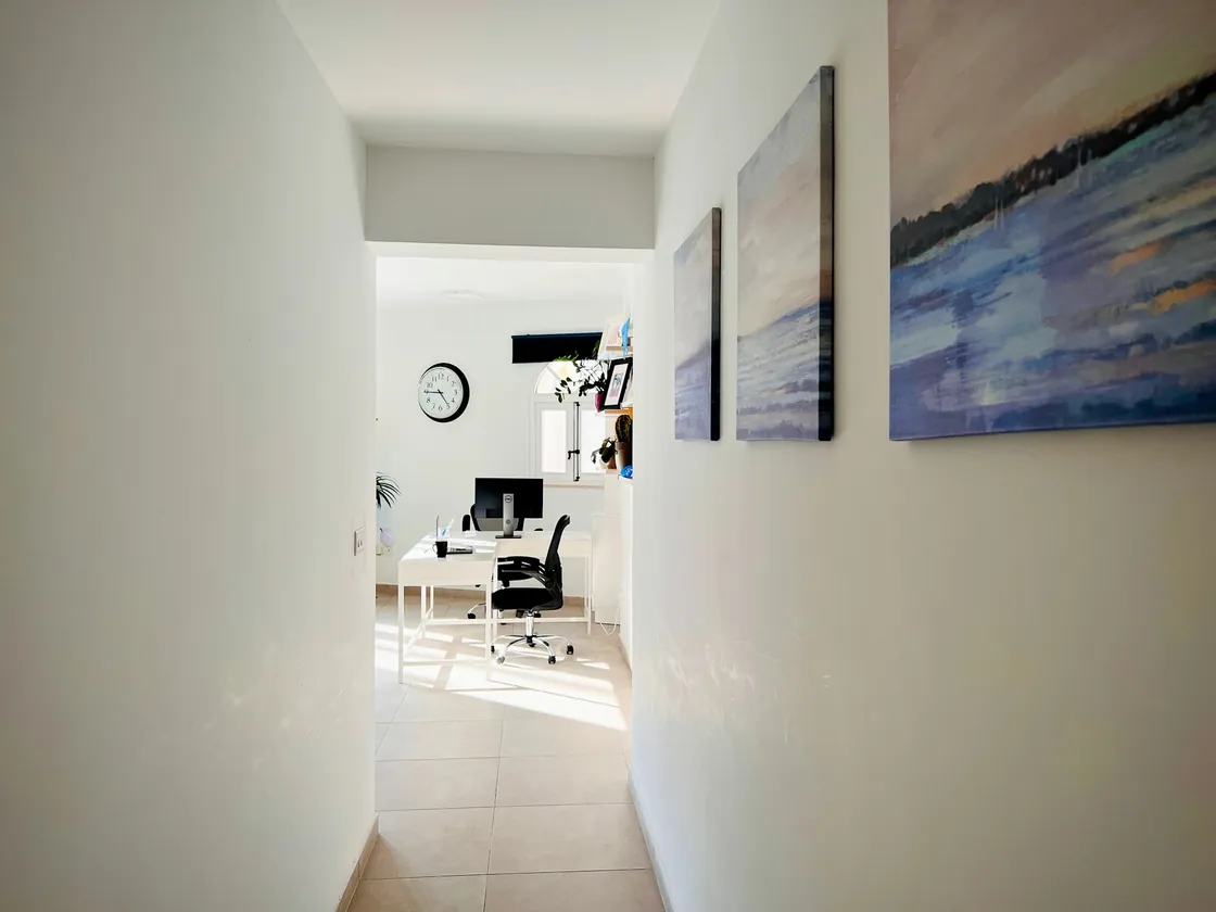 A bright office corridor with framed artwork and a workspace beyond