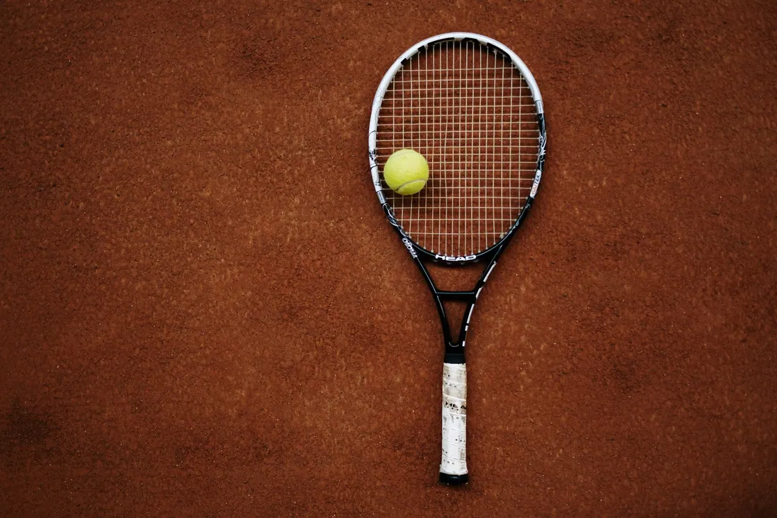 A tennis racket and tennis ball on a clay court