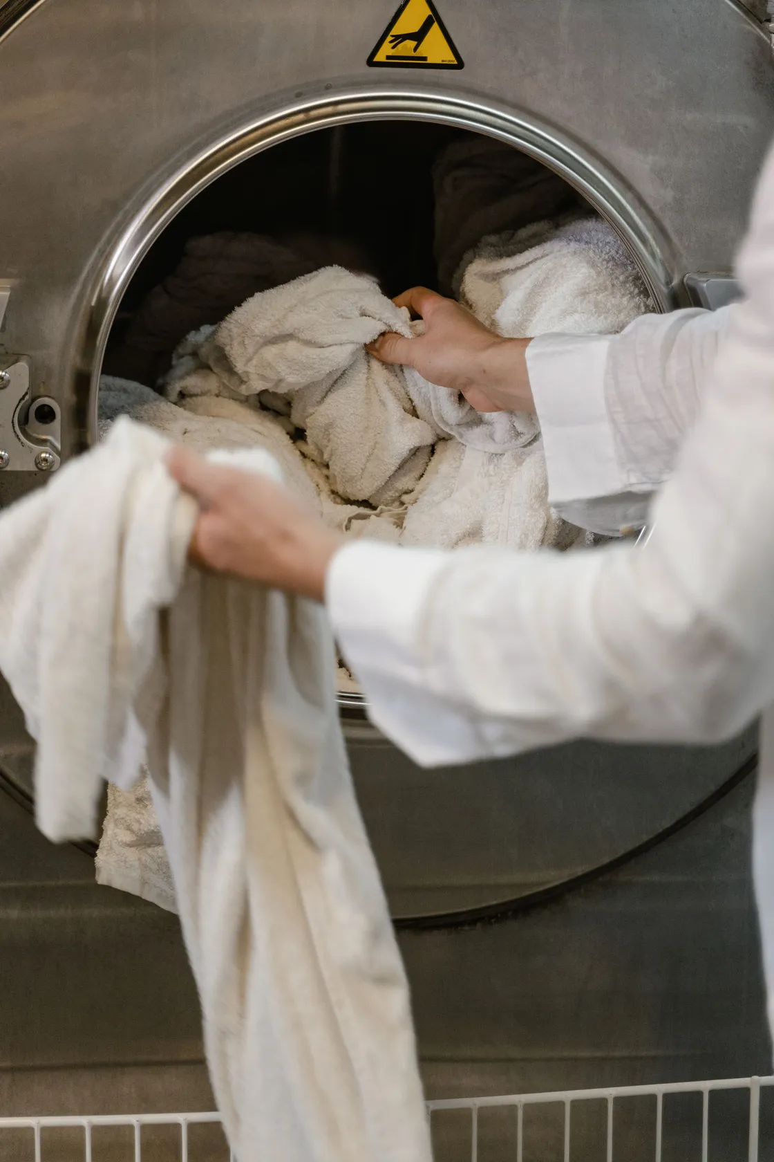 Hands loading light-coloured towels into a laundry machine
