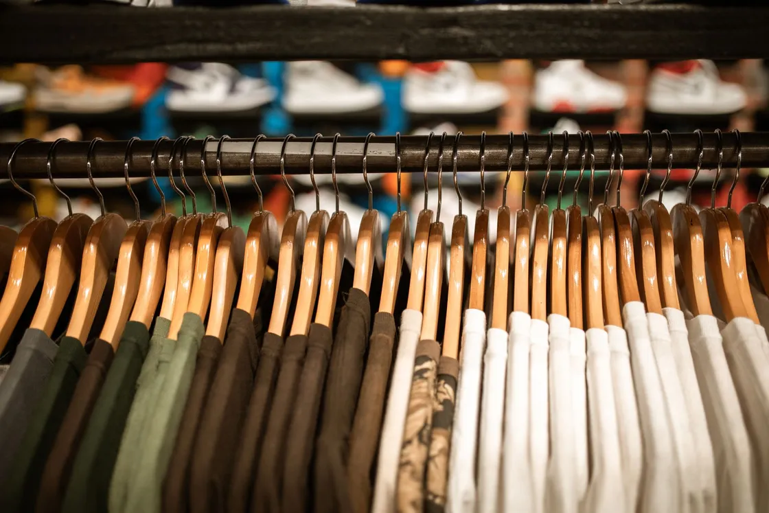 A rail of garments on wooden hangers, arranged from dark to light