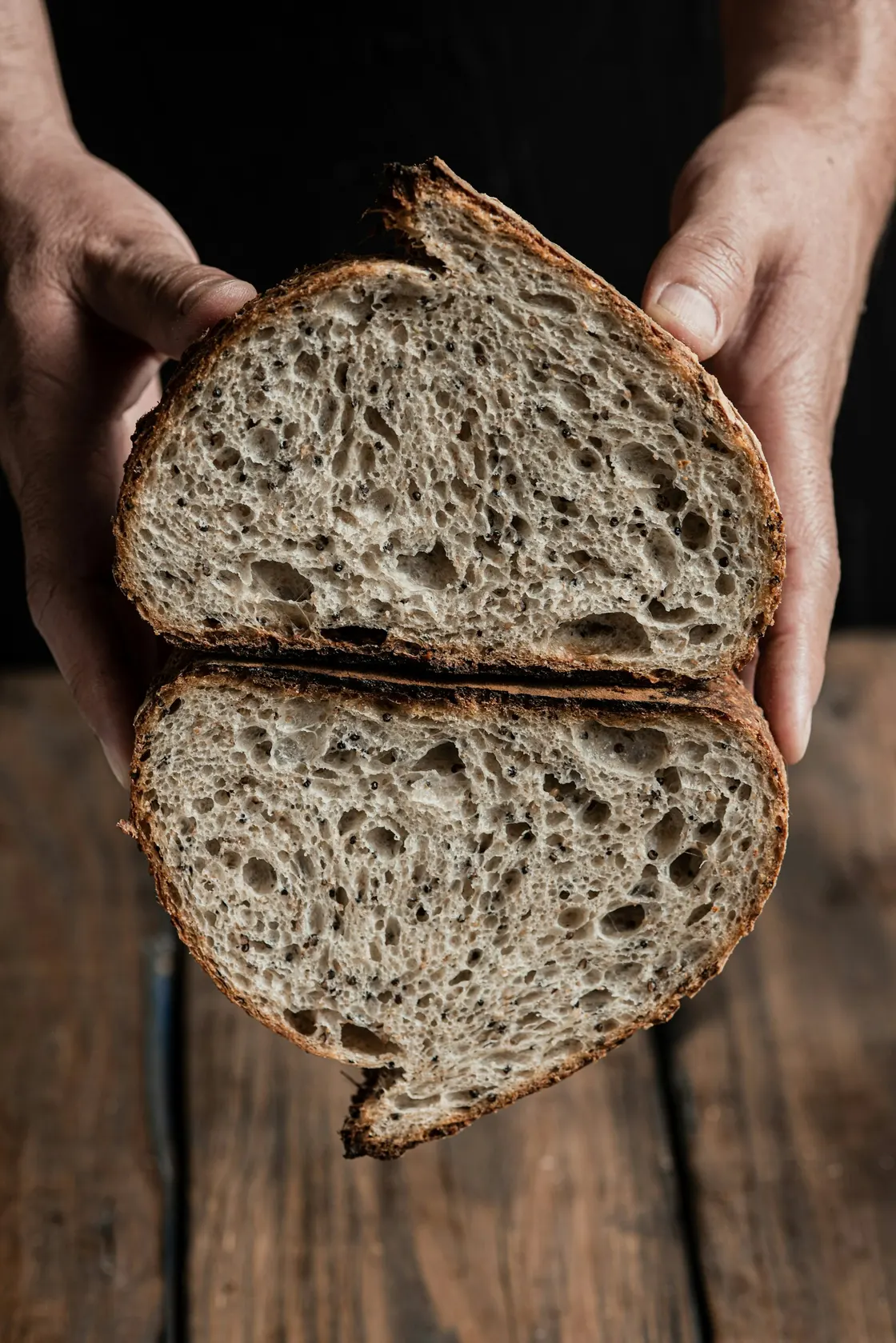 Hands holding two halves of a sourdough loaf, showing the open crumb