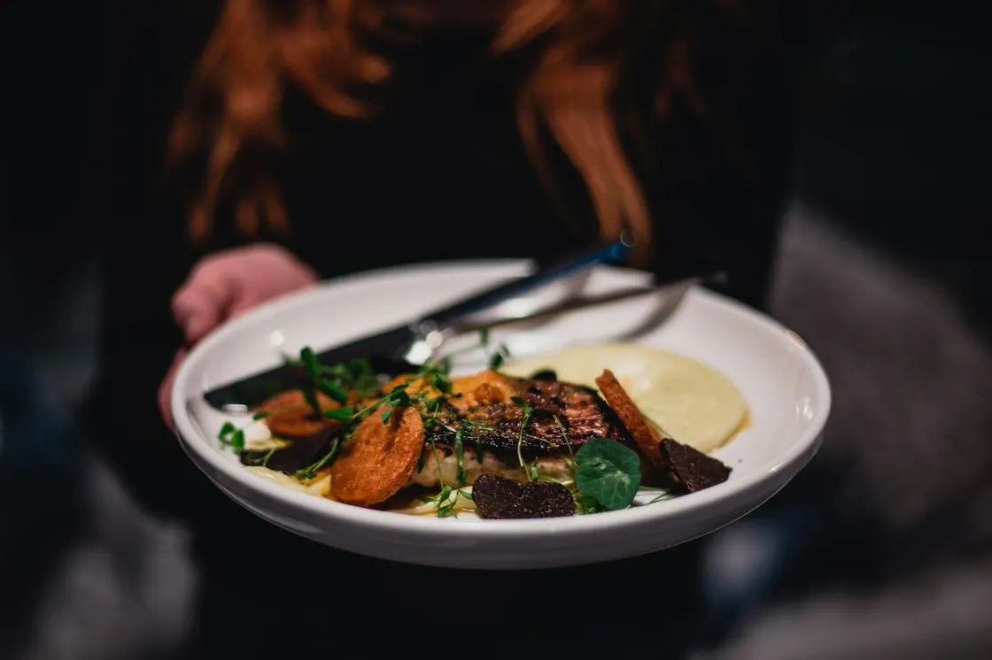 A person carrying a freshly prepared dish on a white plate