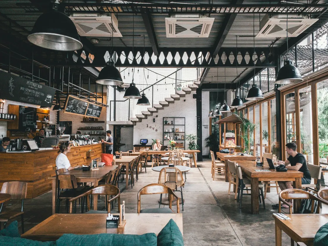A bright dining room with wooden tables, a counter and large windows