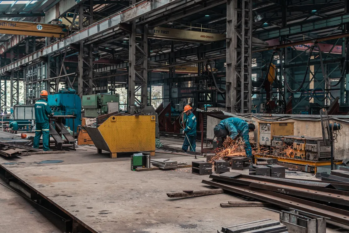 Workers and industrial equipment on a large metal workshop floor