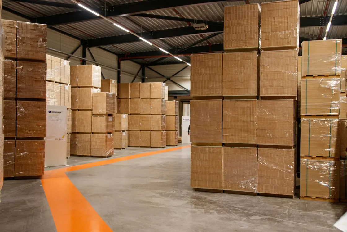 Cardboard boxes stacked within a high-roofed industrial warehouse