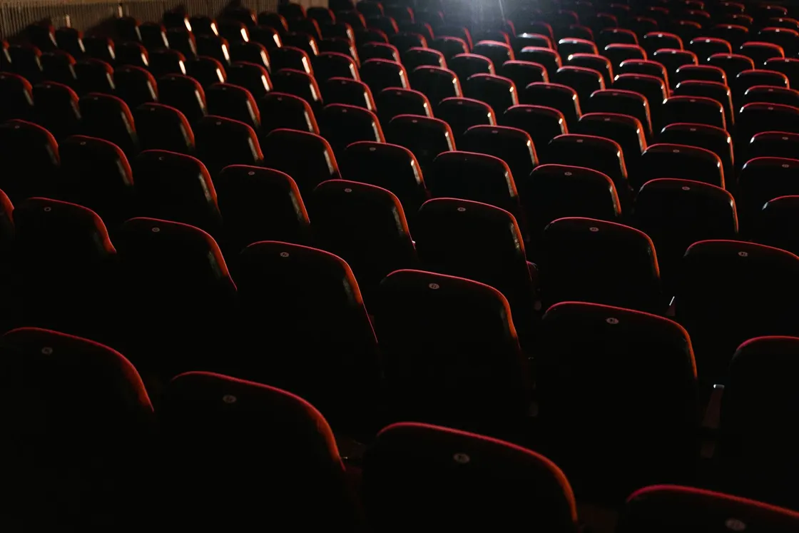 Rows of empty red upholstered seats in a dark cinema auditorium
