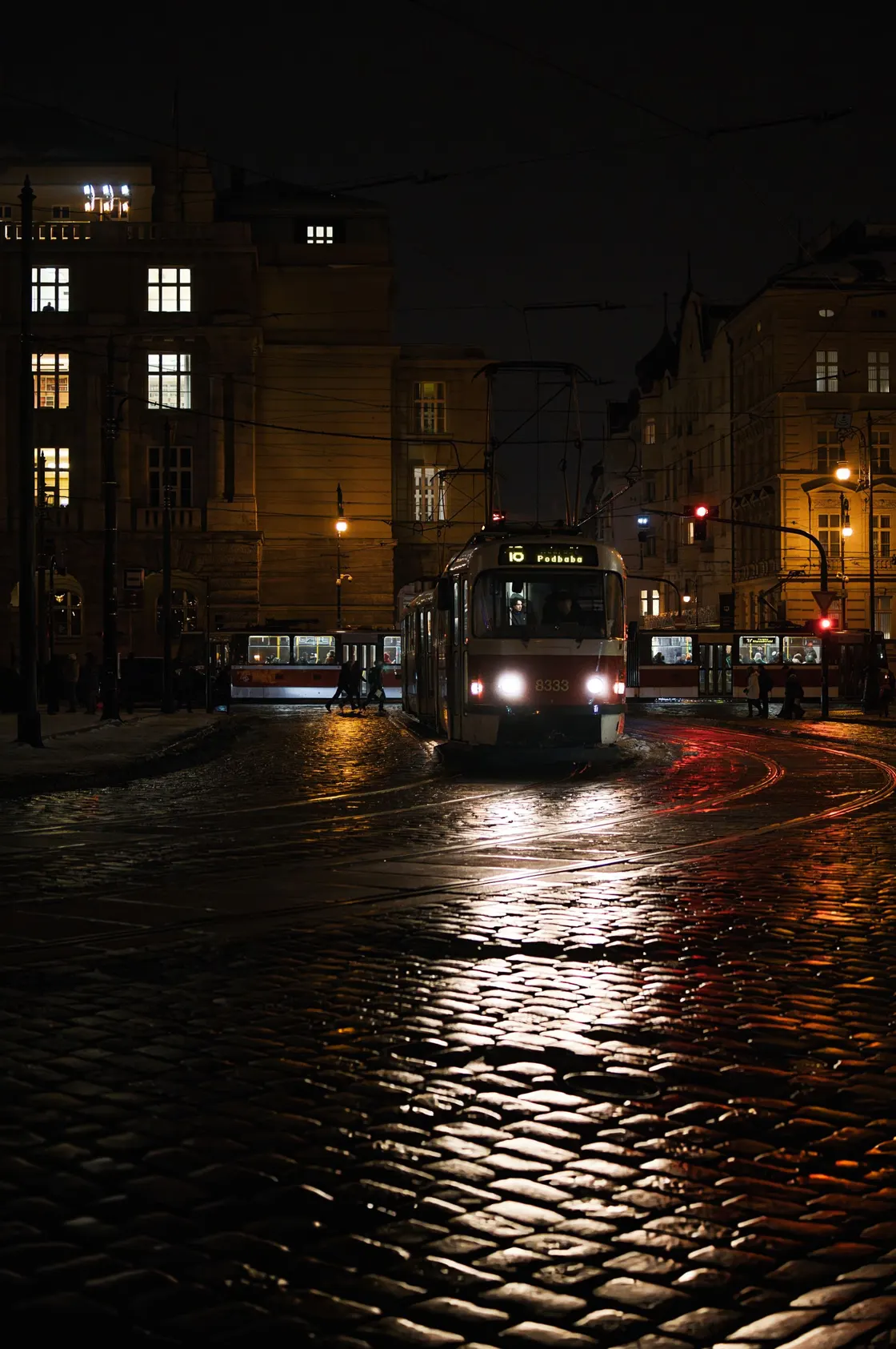 A tram travelling along a wet, illuminated city street at night