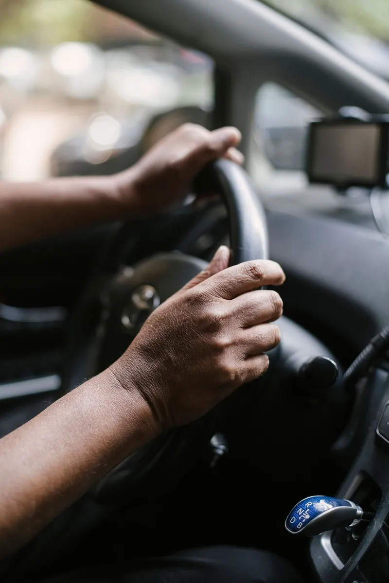 Close-up of hands on a steering wheel with an automatic gear selector in the foreground