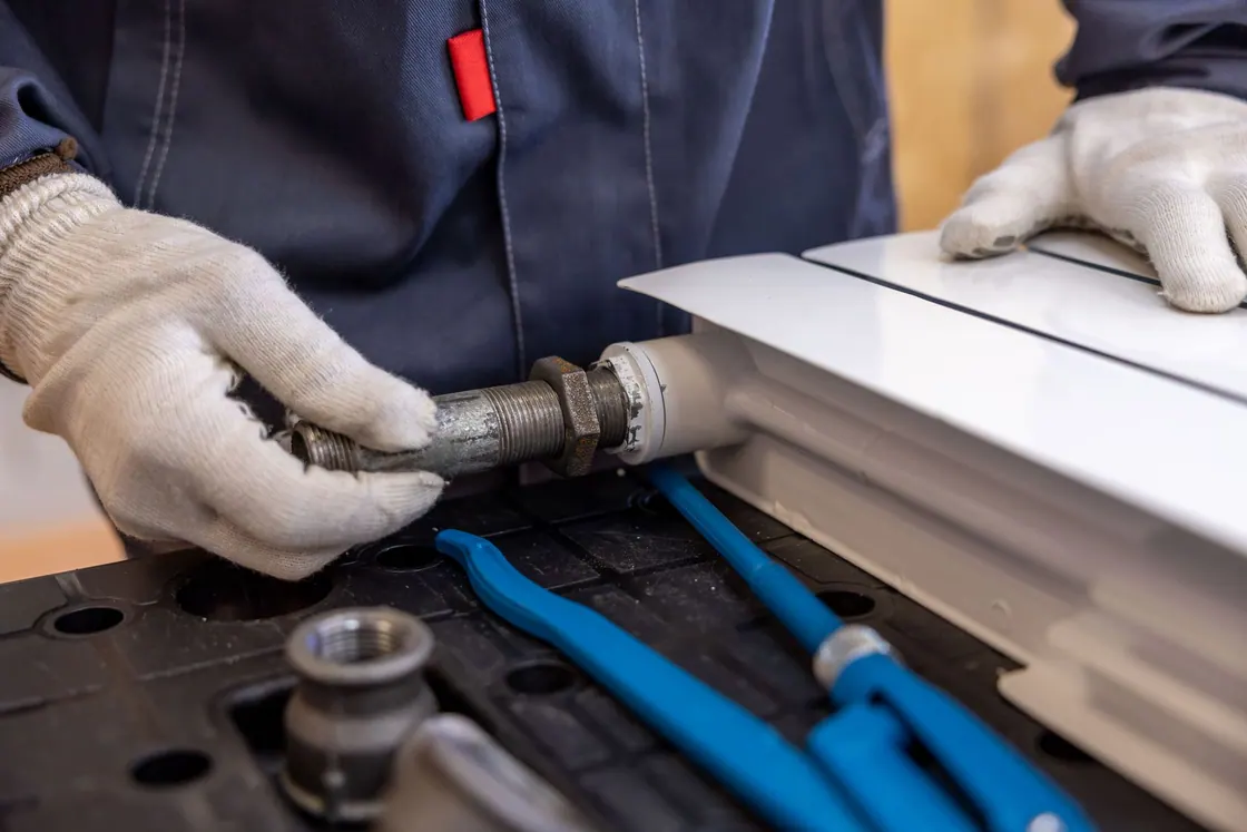 A plumber using tools at a radiator pipe connection