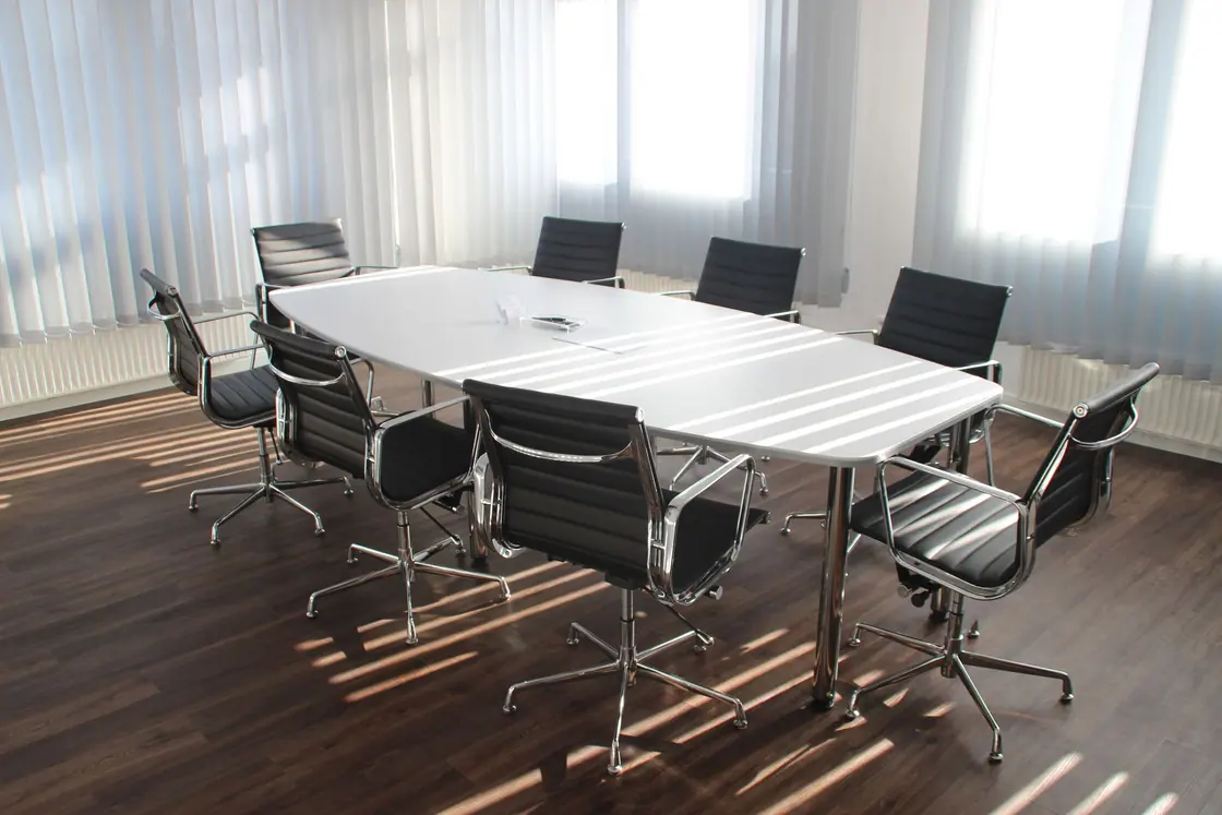 A bright office room with long tables and chairs beside large windows