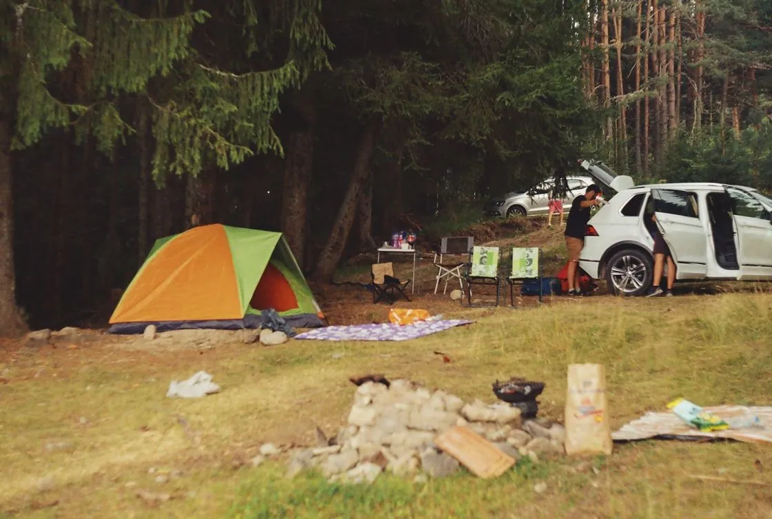 A tent and car among trees in a woodland campsite