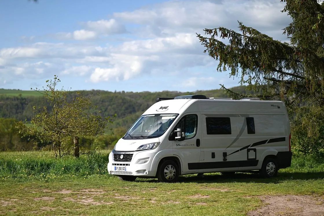 A white camper van parked on grass near trees