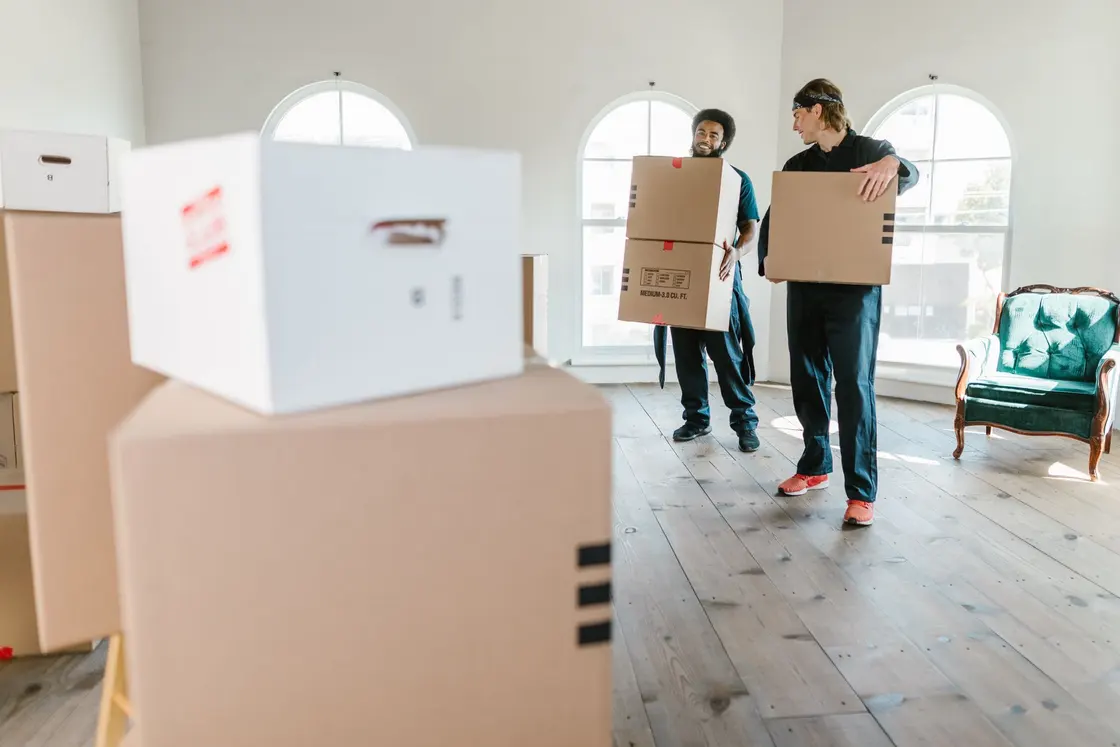 Movers carrying boxed belongings in a sunlit room
