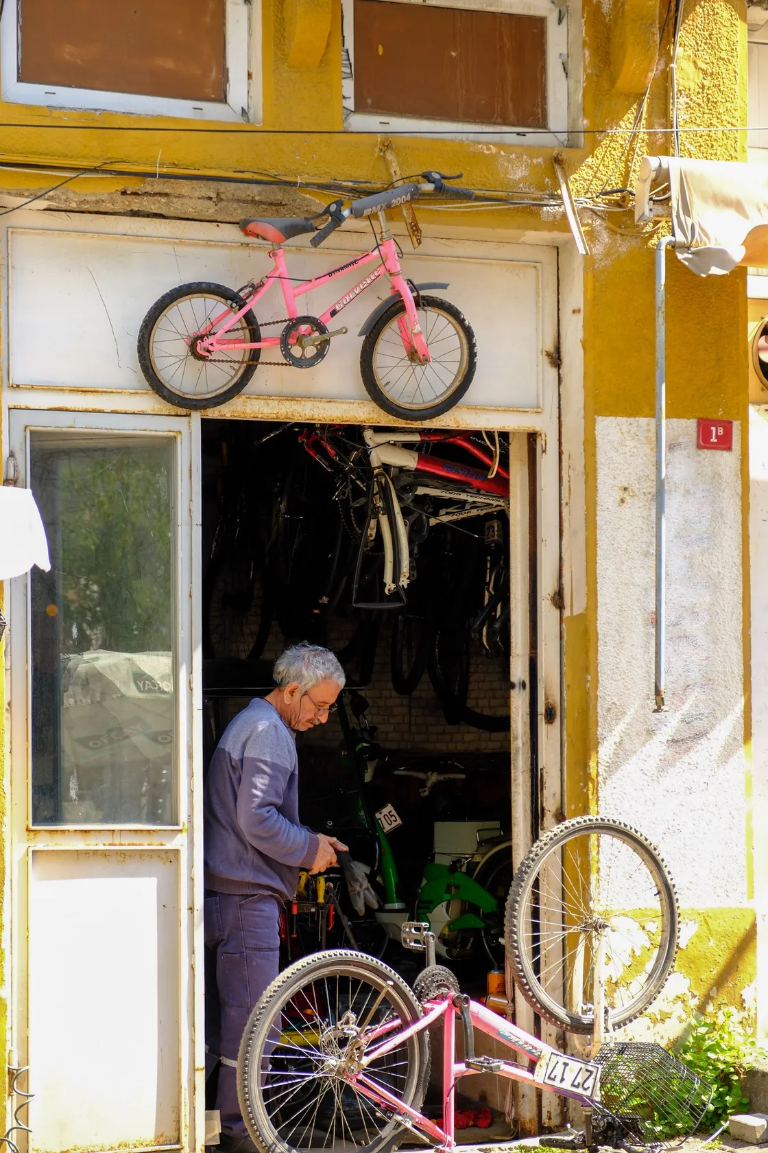 Mechanic working among bicycles outside a yellow-fronted repair shop