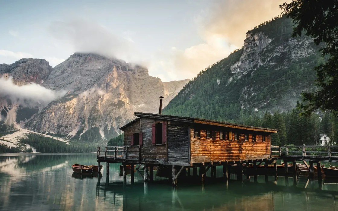 Wooden boathouse reflected in a mountain lake with low clouds above the peaks
