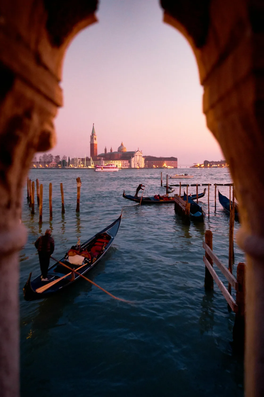 Gondolas and the waterfront of Venice seen through an arched stone opening at dusk