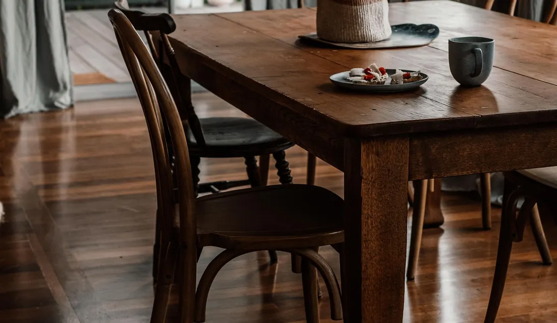 Warm wooden dining furniture beside a window with dark curtains