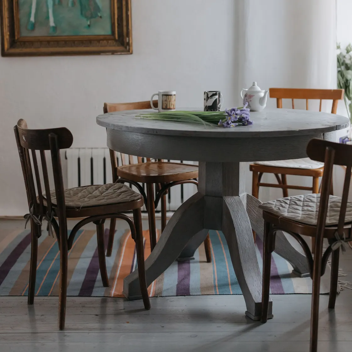 A round grey-painted dining table with mixed wooden chairs