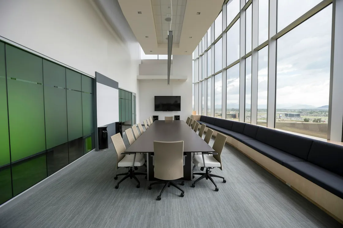 A wooden conference table and chairs beside large windows